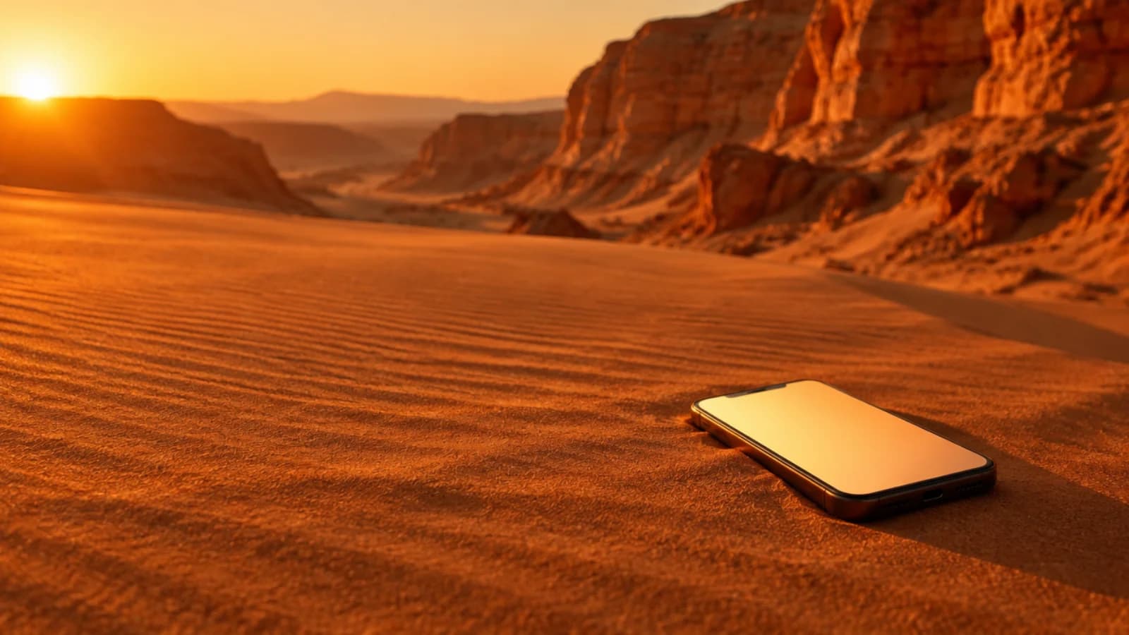Celular com a tela acesa sobre a areia do deserto ao pôr do sol, com cânions ao fundo